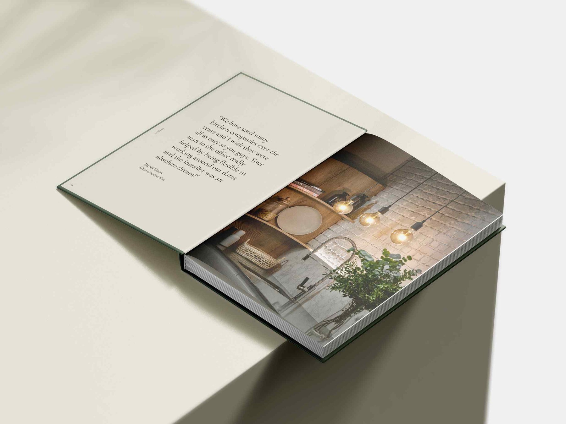 Academy Kitchens brochure open at a client quote spread facing a photograph of a kitchen with exposed brick and glass pendants, print design by HDEY