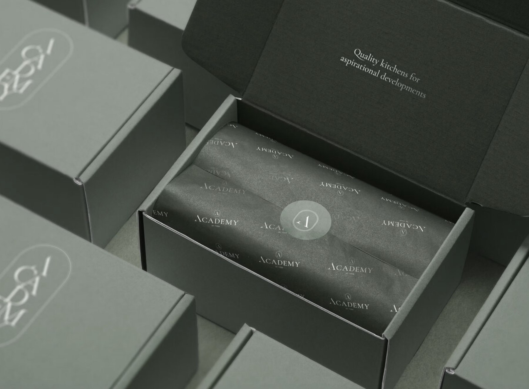 Academy Kitchens sample boxes in sage green with the debossed logomark, branded tissue paper and the strapline printed inside the lid — packaging design by HDEY