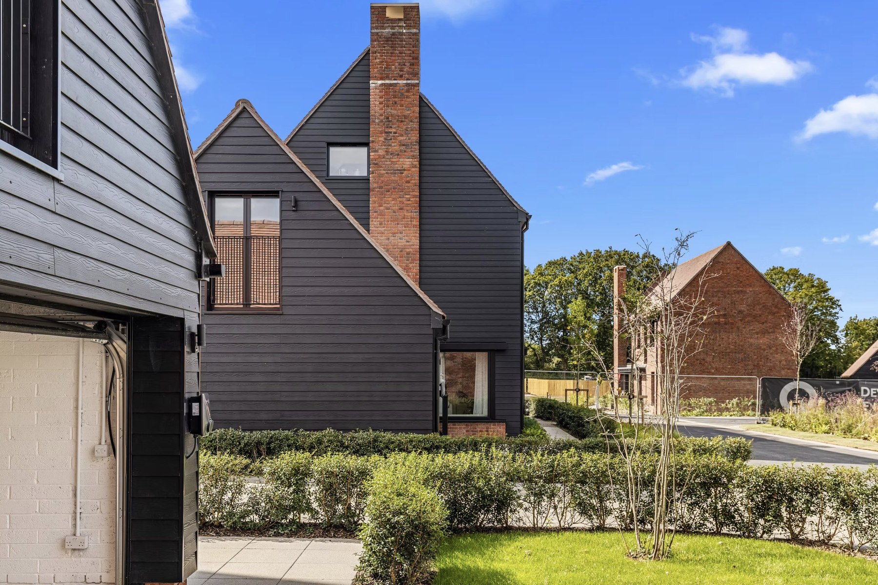 Alfold Gardens exterior detail with dark timber cladding and brick chimney, Surrey