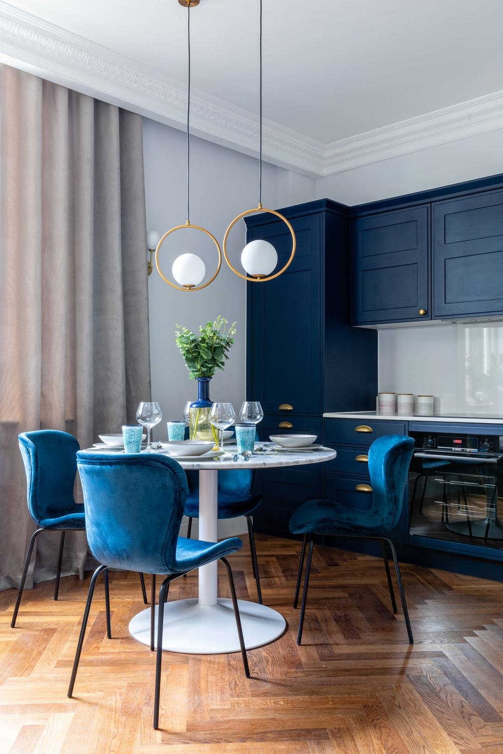 The Chalk Lane Residences show home kitchen and dining with navy cabinetry, teal velvet chairs and brass pendants, Epsom — by HDEY