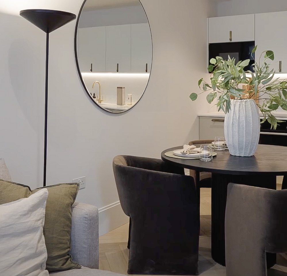 Ealing Broadway show home living and dining space with a pale sofa, olive cushions, dark dining table and the kitchen beyond, West Ealing W13 — interior design by HDEY