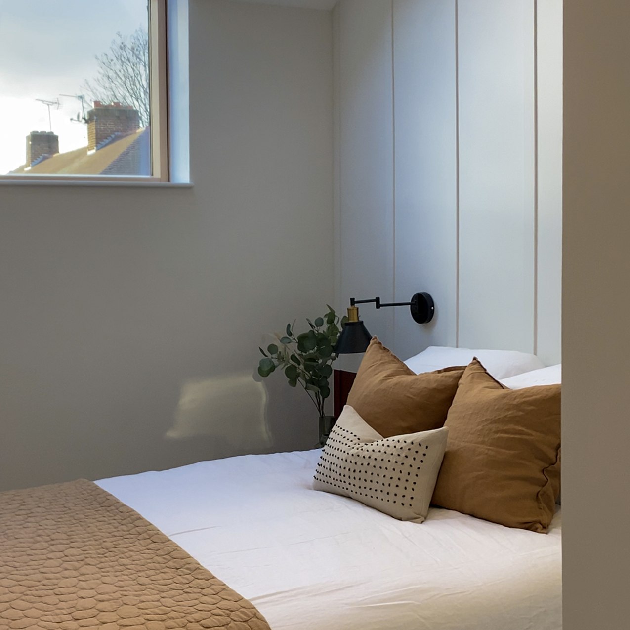 Fifty One bedroom as built, with the panelled headboard wall, a swing-arm wall light and tan linen, Ealing