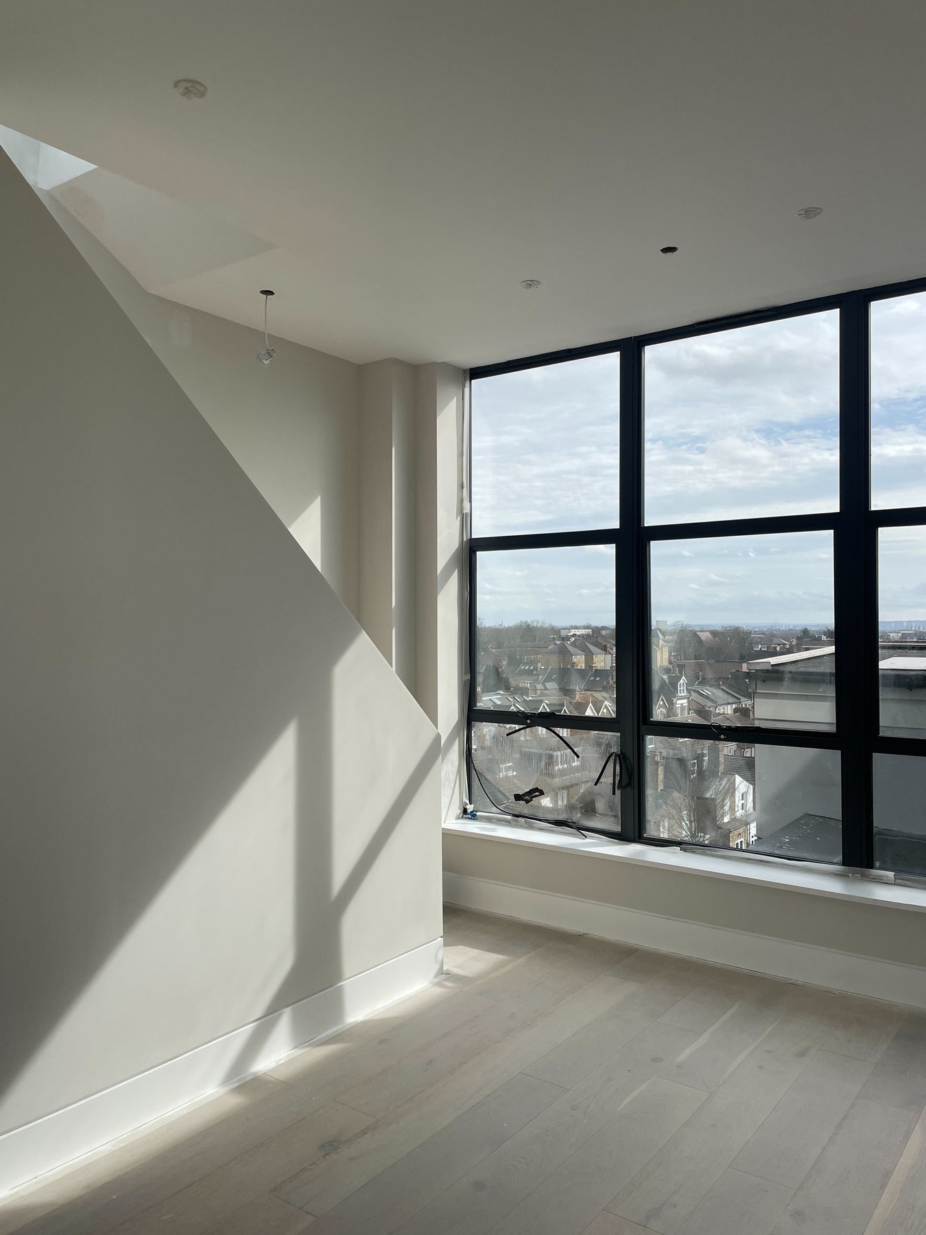 Q17 Lofts apartment as built, with the pitched ceiling, full-height black-framed glazing and rooftop view over Walthamstow