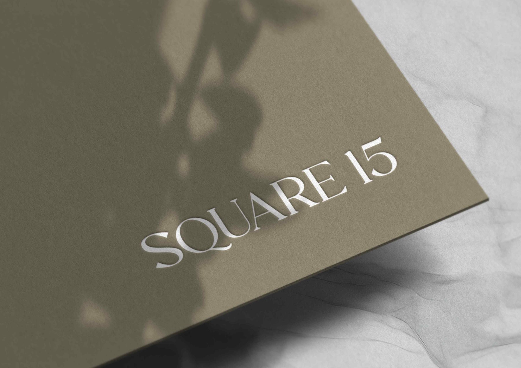 Square 15 logotype foiled in white on an olive stock, with leaf shadow falling across it, brand identity by HDEY