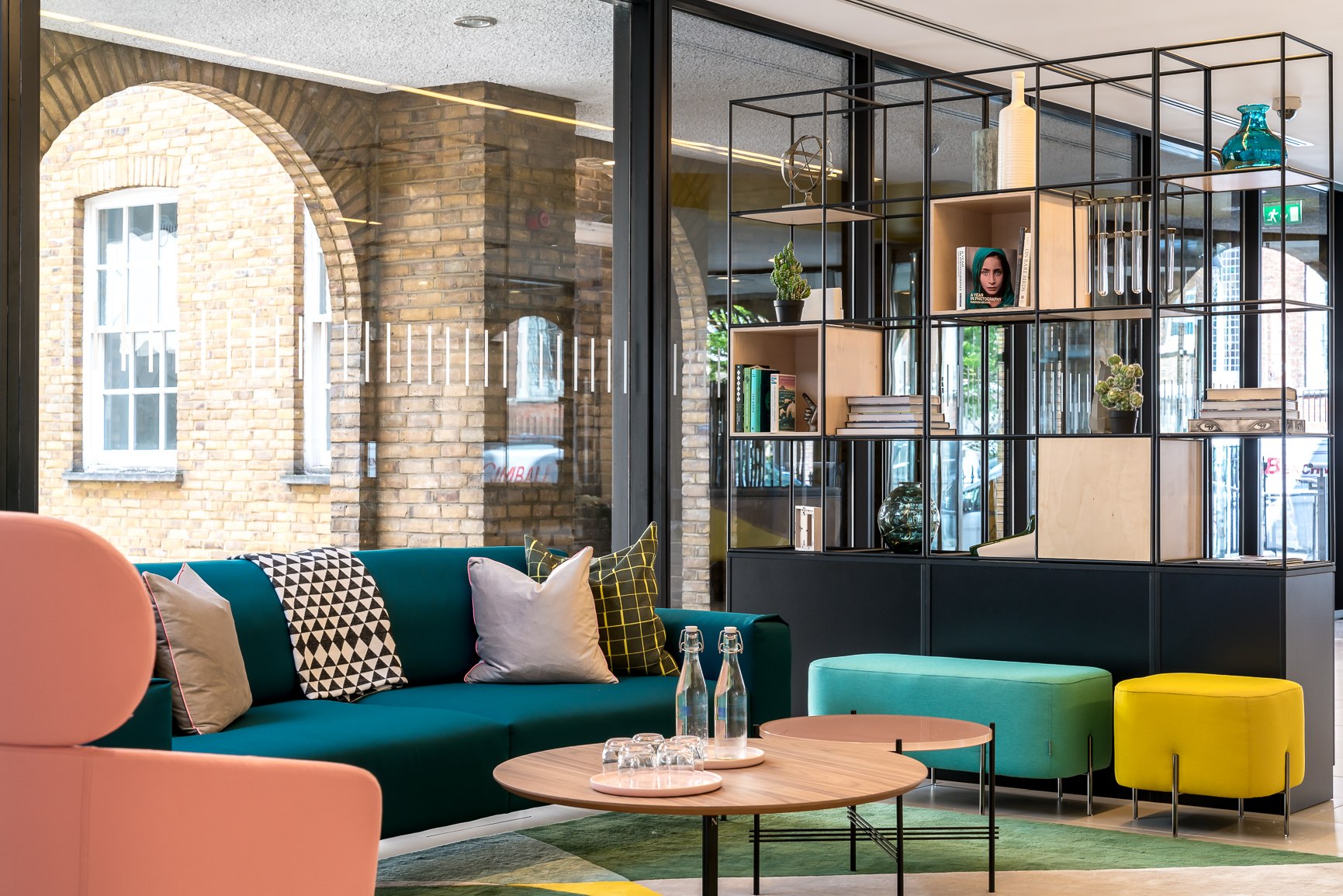 Twenty lounge seating with teal sofa, coral chair and round tables, arched brickwork beyond the glazing, London Bridge — by HDEY