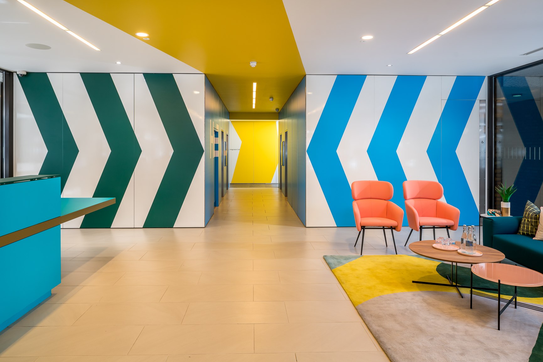 Twenty reception at New City Court, London Bridge, with teal, blue and yellow chevrons applied to white walls and coral armchairs — interior design by HDEY