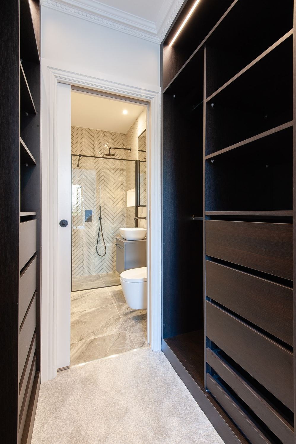 West Lodge walk-in wardrobe in dark joinery opening to the ensuite, Ealing — by HDEY